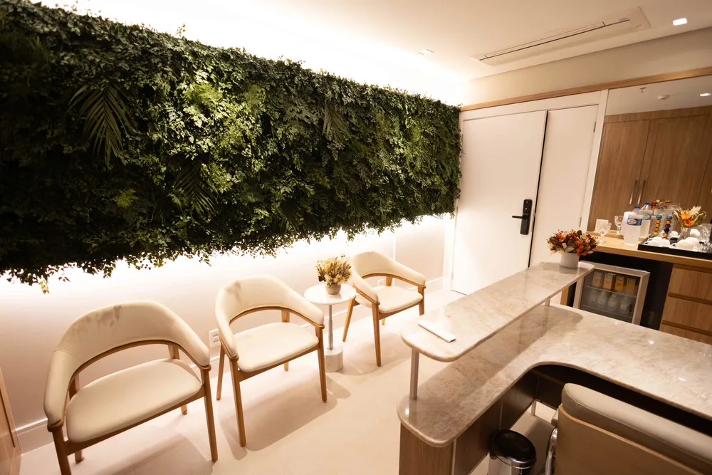 Sala de espera com parede verde, poltronas claras e cantinho de café